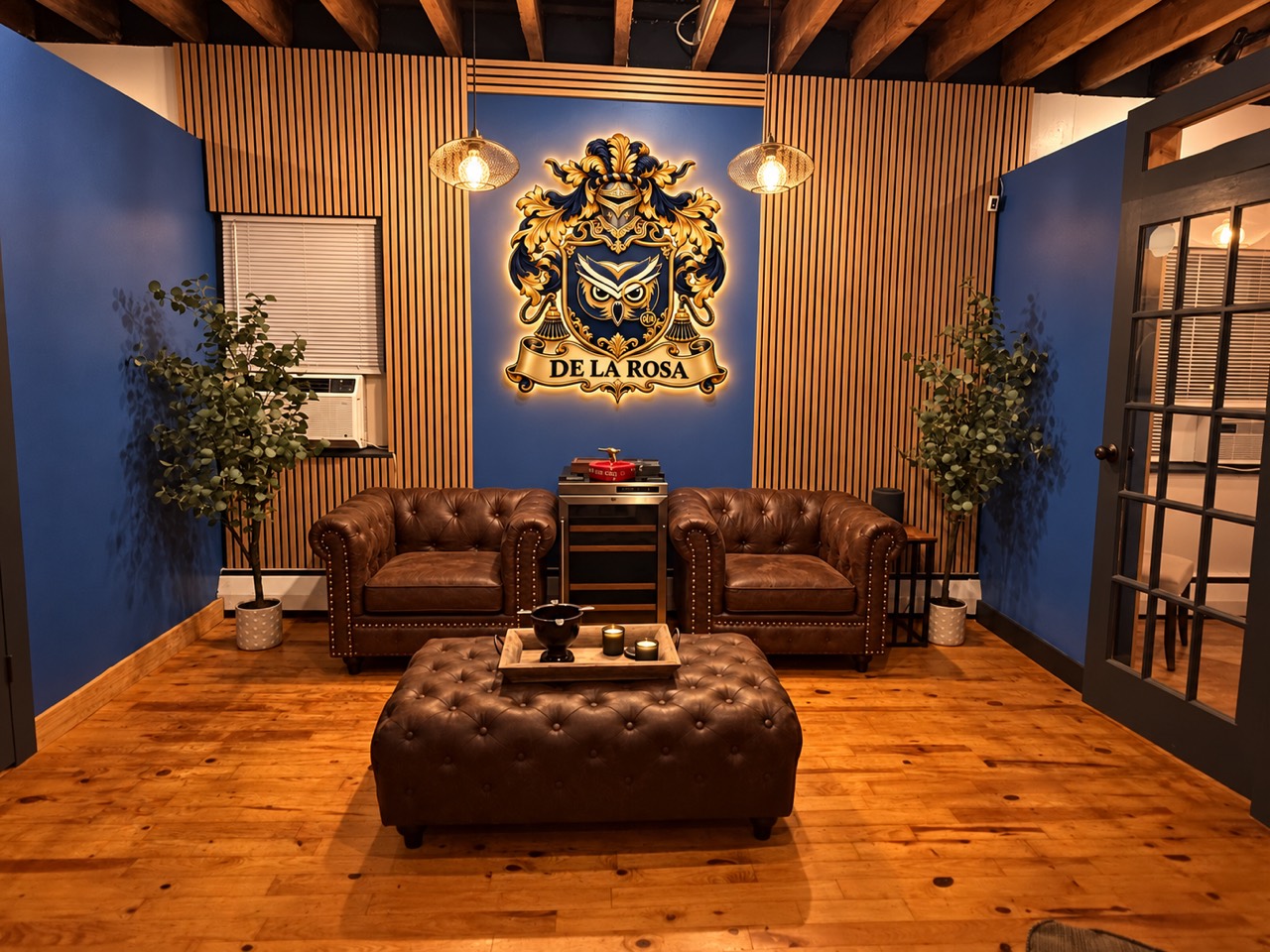 The DLR Bronx office lounge with its gold De La Rosa owl crest, navy walls, wood-slat panels and brown leather chairs.